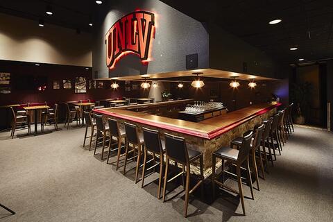 Small bar completely surrounded by a high table and chairs, a large u-n-l-v logo on the wall behind the bar