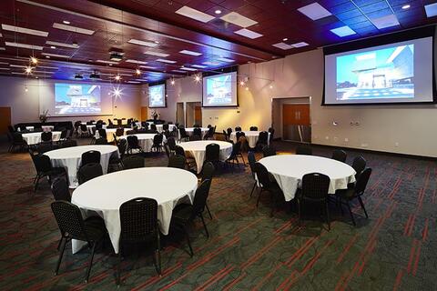 Large ballroom with numerous round table evenly spaced out, each table has a white table cloth and black chairs