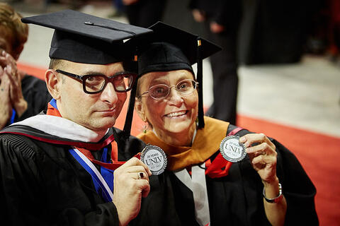 Two graduates hold up badges.