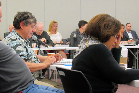 Man typing and a woman taking notes in a boardroom full of people in professional clothing