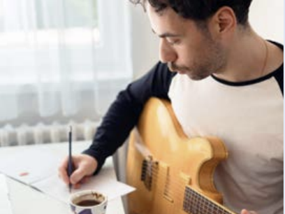 A man writing music and playing guitar