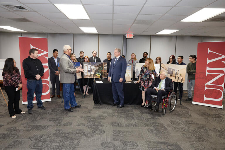 Al Gore, Senator Harry Reid, and President Marta Meana stand with a group of 15 students and their advisor in front of posters with drawings for a solar home.