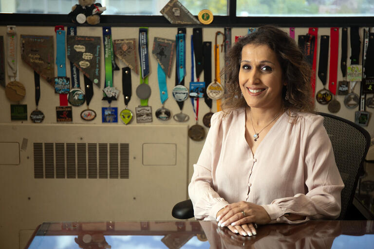 A woman sits at a desk, in front of a row of medals