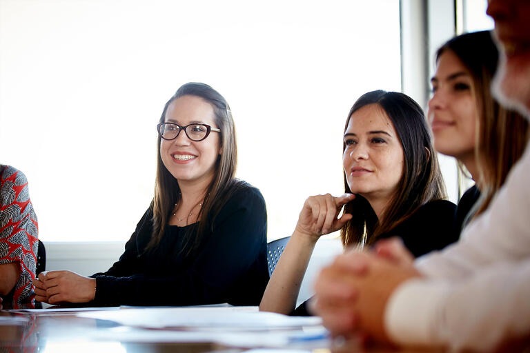 A woman smiles while sitting at a conference table