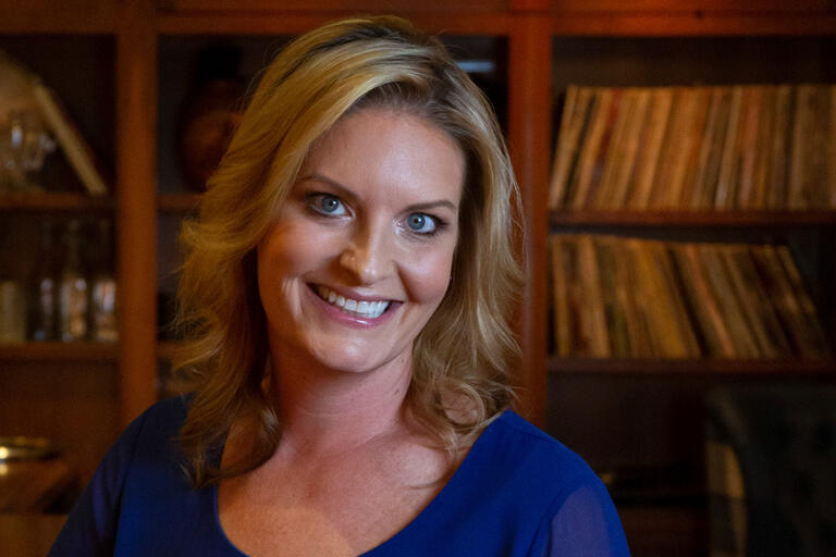 A woman in a blue dress stands in front of bookshelves