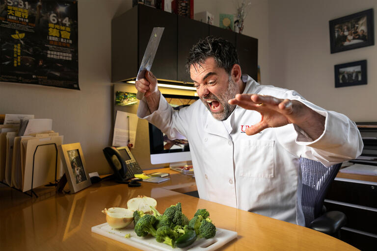 A chef raises a cleaver to chop and onion and broccoli.