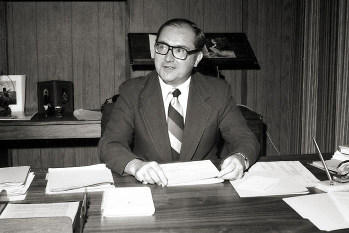 Man wearing a formal suit sitting in his office handling a small pile of papers.