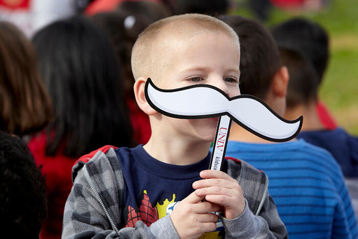 Young boy holding up a Hey Reb paper mustache to his face.
