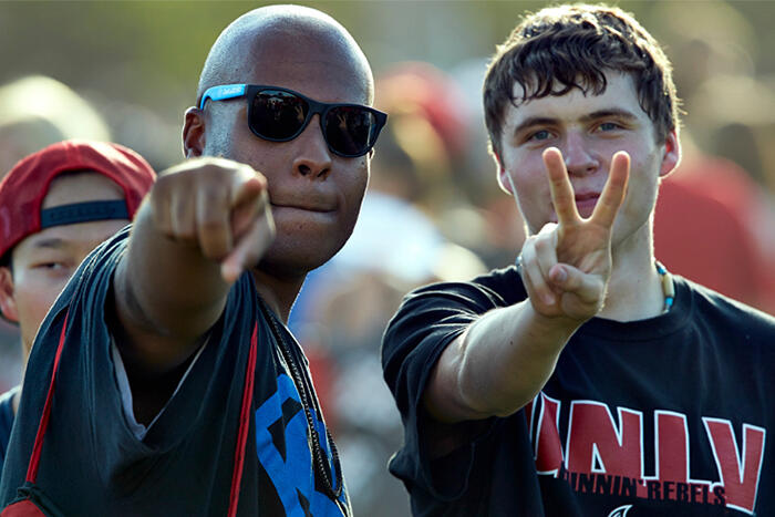 Front side view of two guys giving hand gestures to the camera. One is pointing, the other giving the peace sign.