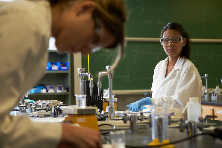 Two students in lab coats and goggles attend an organic chemistry lab class