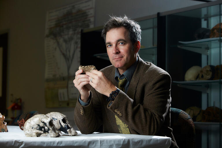 Brian Villmoare sits at a desk and holds a fossil