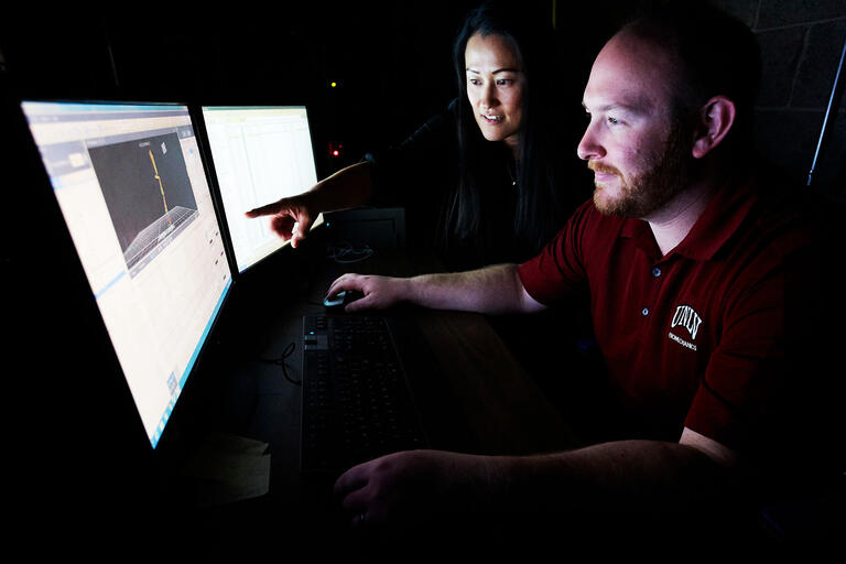 woman pointing at computer with man looking on.