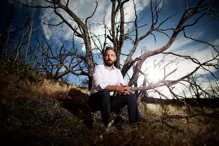 man sitting between burned trees.