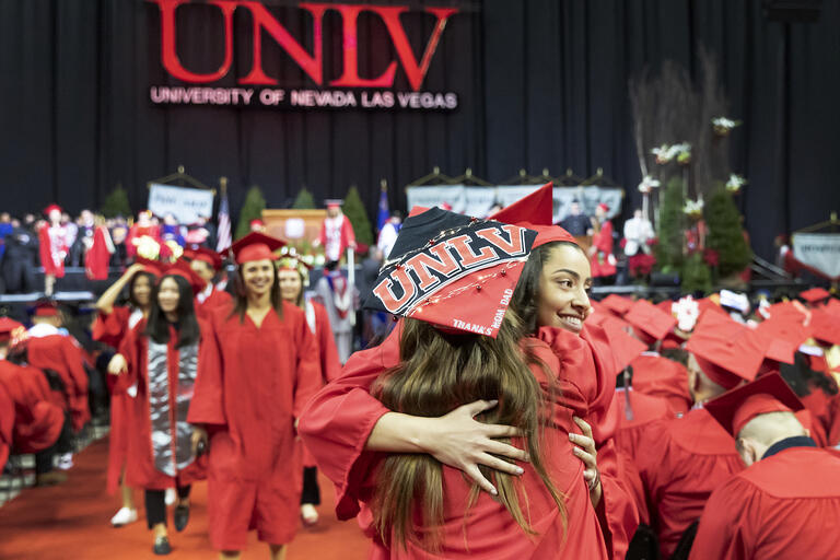 UNLV students in red caps/gowns hugging at commencement
