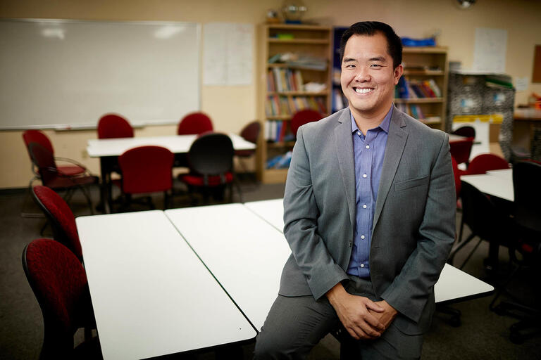 Frederick Ngo poses in front of tables and chairs in a classroom.