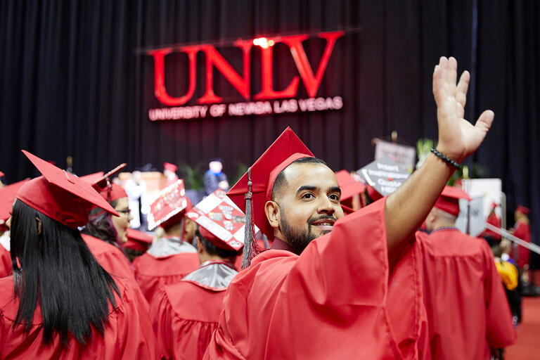 UNLV student in cap and gown waves to crowd during commencement