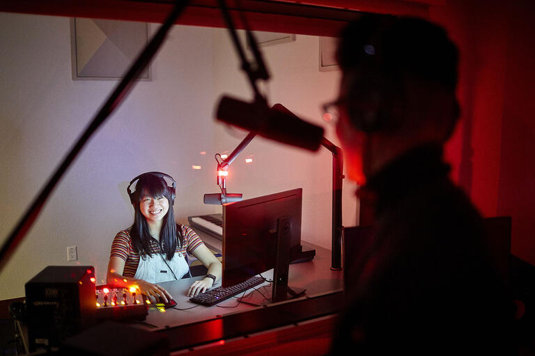 woman in audio recording studio looking through window at performer