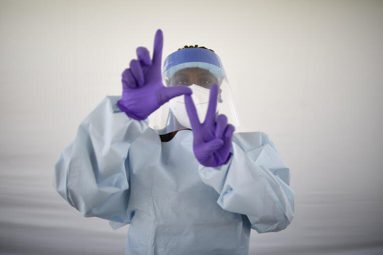 medical worker in full protective suit making &quot;LV&quot; sign with hands