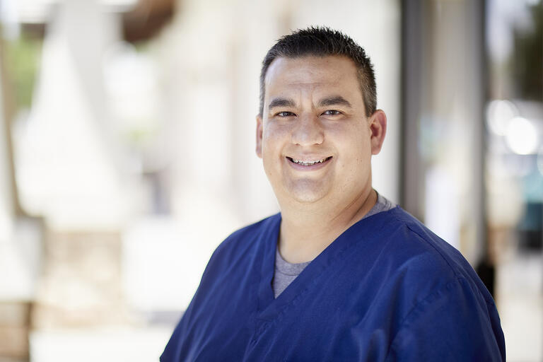 Portrait of Dr. Daniel Diaz wearing blue scrubs. Diaz is playing a key role in day-to-day operations at UNLV Medicine's COVID-19 curbside test operation