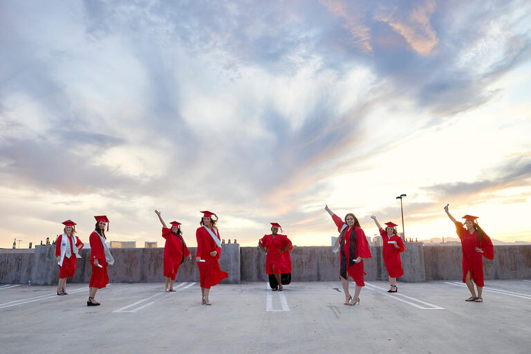 Eight UNLV graduates pose for a photo in their graduation attire.