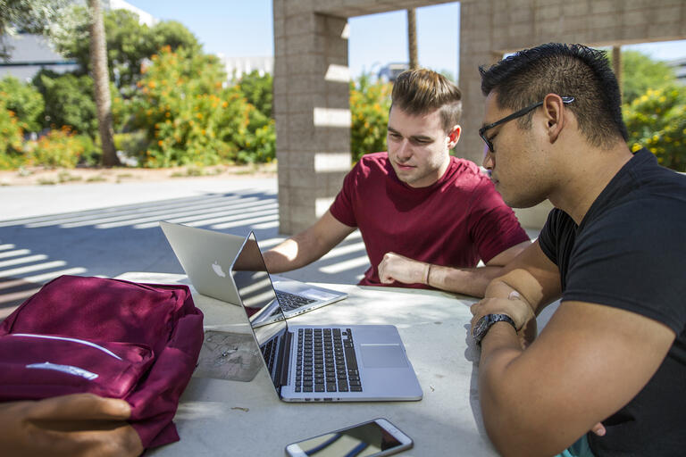 two young men studying with laptops