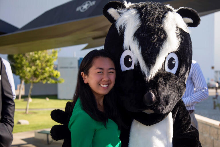 A woman stands next to a mascot in a skunk costume