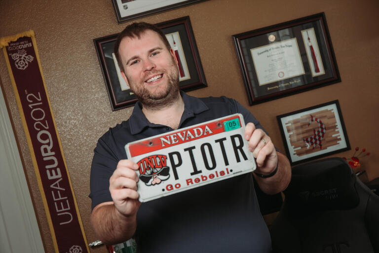 A man holds up a UNLV license plate reading &quot;Piotr&quot;