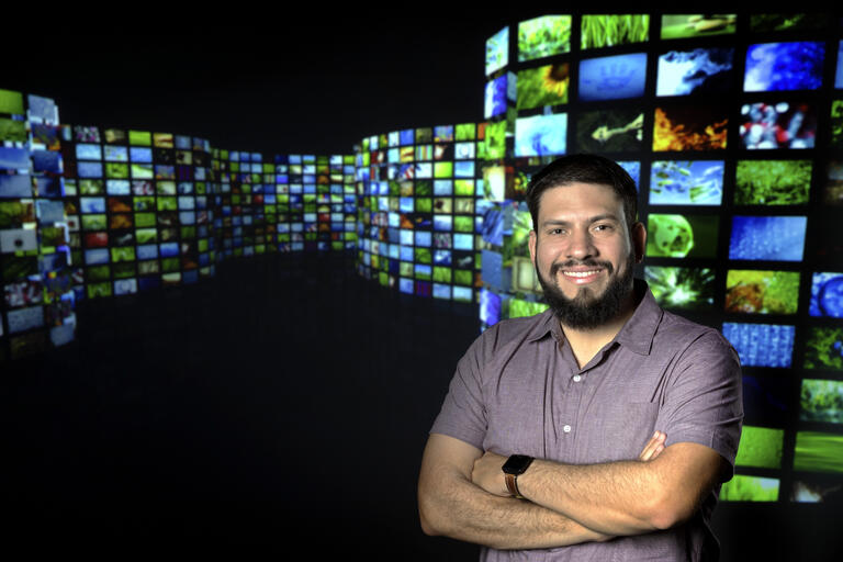 Carlos Flores stands in front of a bank of television screens