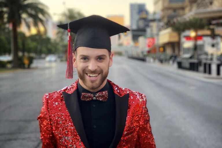 Ryan wears a black grad cap and a sequin jacket standing on an empty Las Vegas strip.