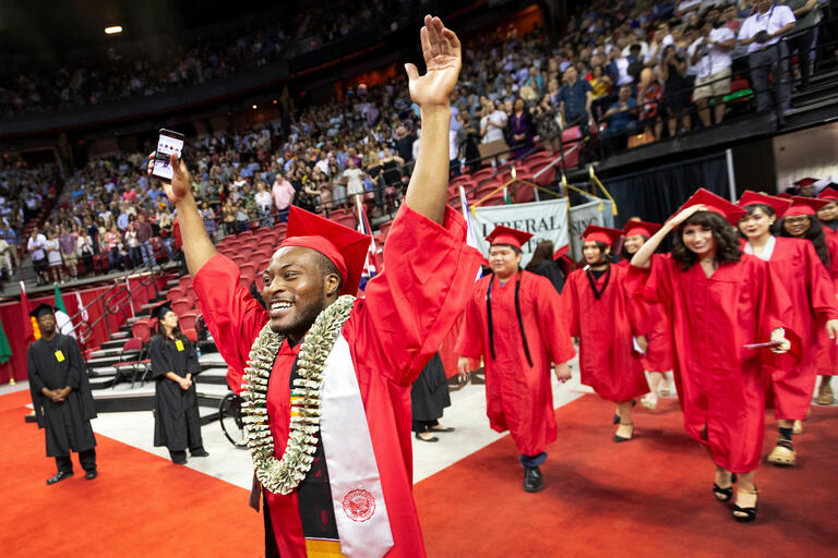 A student raises his arms in celebration at commencement