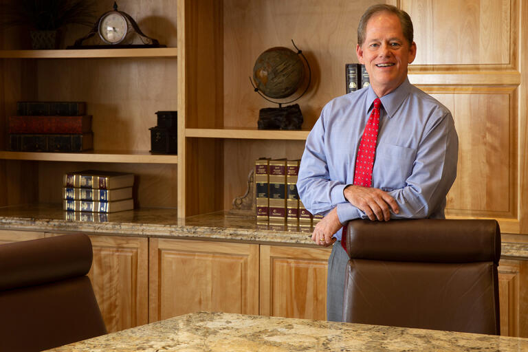A man in  a blue shirt stands behind a chair.