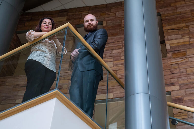 A man and a woman stand on a balcony looking down.
