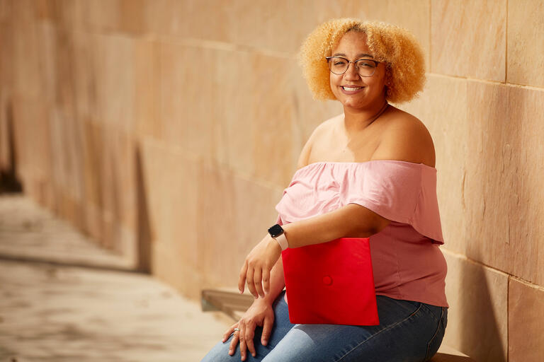 A young woman holds a red mortarboard cap.