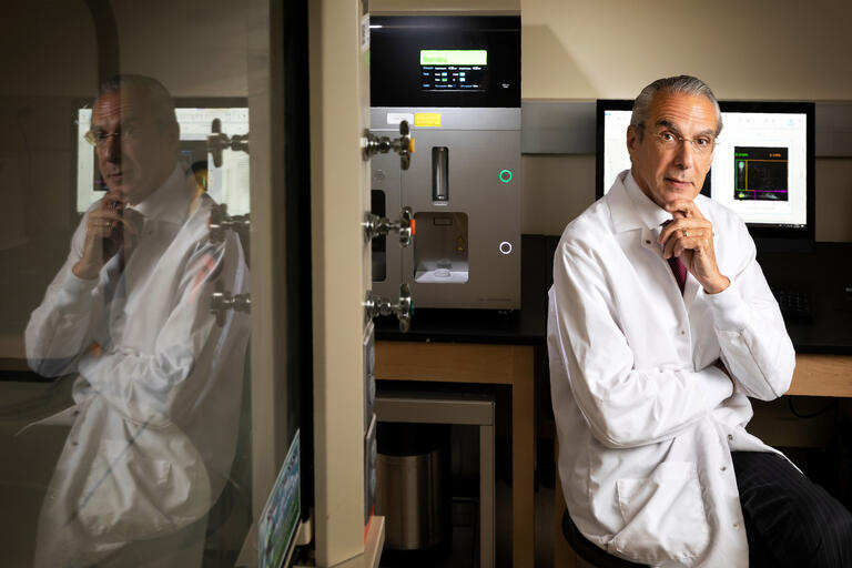 A scientist in a white lab coat rests his hand on his chin