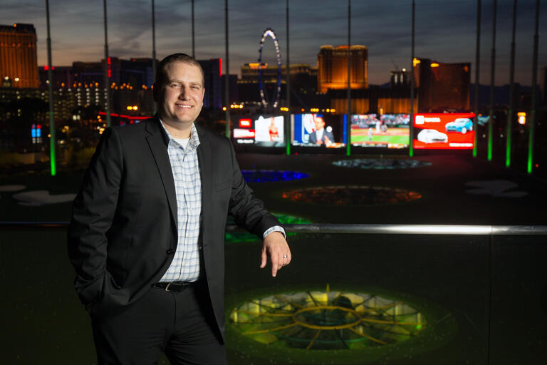 A man stands at a driving range, with a view of the Las Vegas Strip behind him