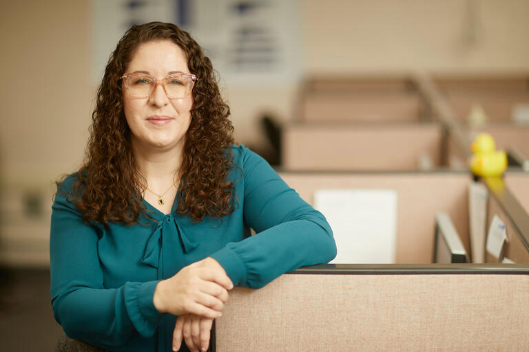 A woman leans on a cubicle wall