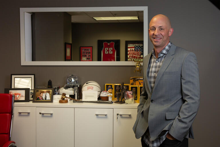 A man in a gray jacket stands in front of UNLV memorabilia