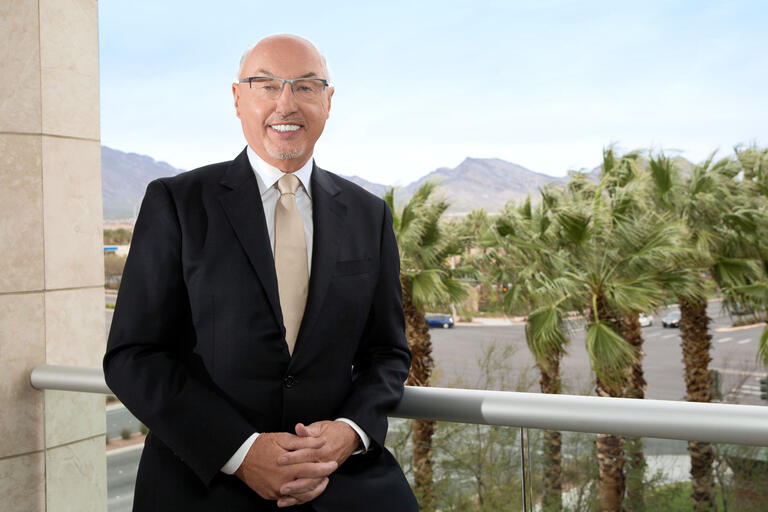 A man in a suit stands on a balcony overlooking the desert