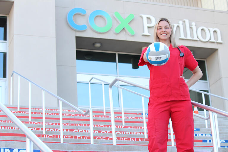 A woman in nursing scrubs holds a volleyball