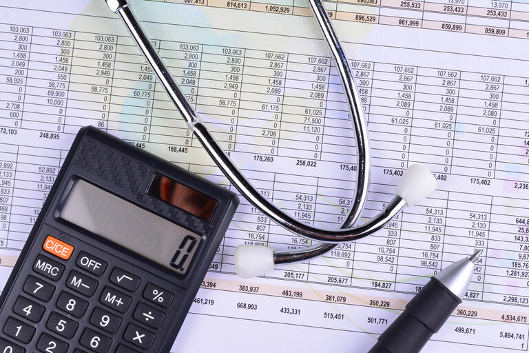 A calculator and stethoscope atop a spreadsheet