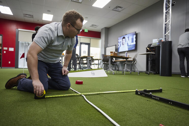 Samuel Masters uses a length of rope to measure out a distance on artificial grass.