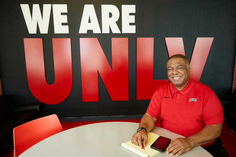 A man sits at a tabel in front of a "We Are UNLV" sign