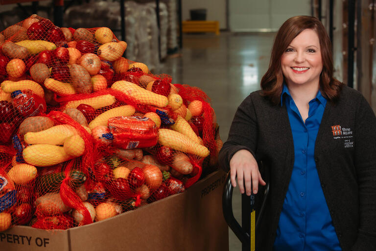 A woman stands next to a large bin holding fresh produce