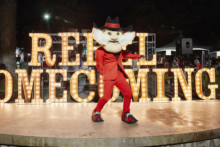 Rebel mascot dancing in front of "Rebel Homecoming" sign