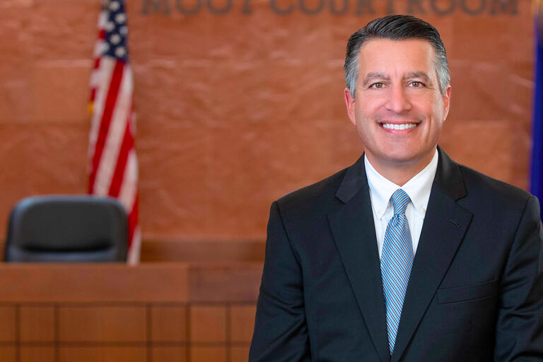 A man in a dark suit smiles in a courtroom.