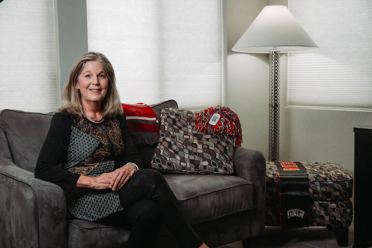 A woman sits on a couch, surrounded by UNLV paraphernalia