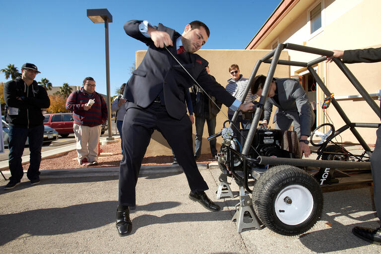 A man in a suit pulls a cord on a dune buggy