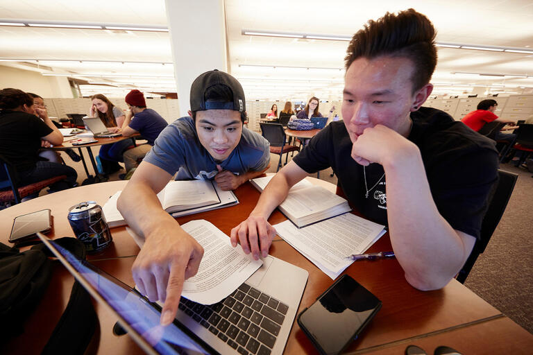 Two students examine a laptop computer in the library