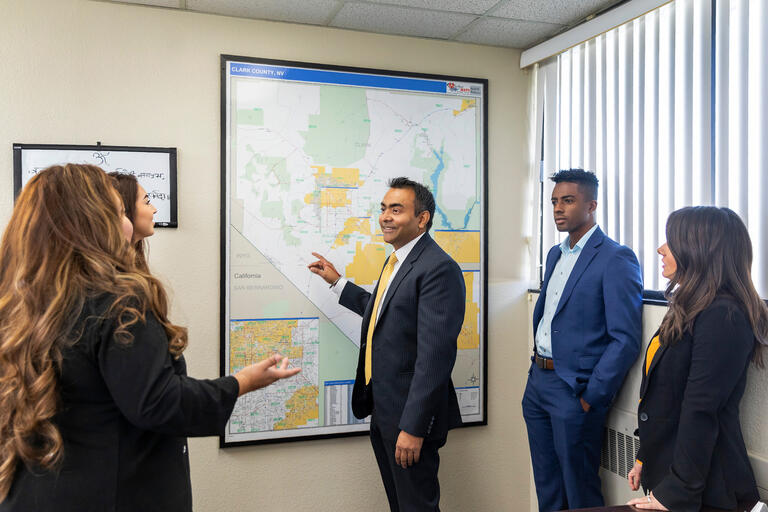A man in a suit points to a map of Clark County as several students look on