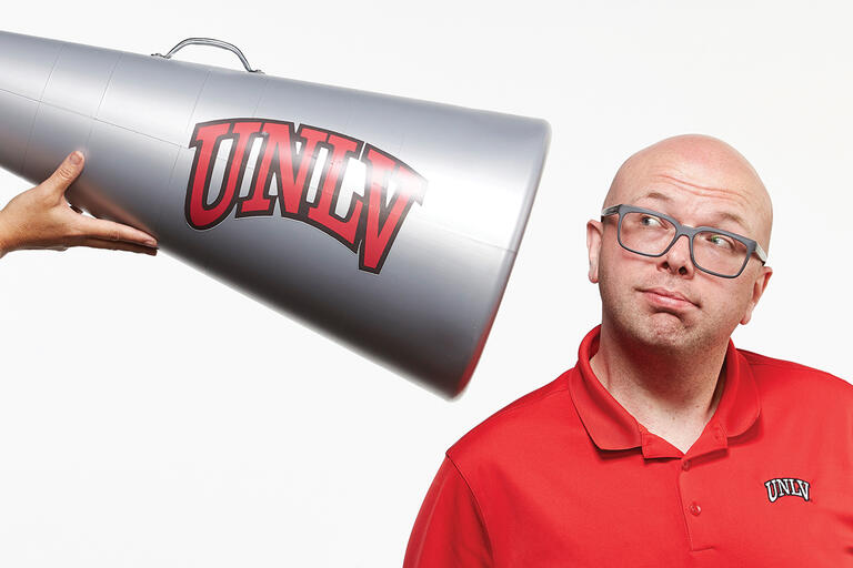 A man leaning into a megaphone that reads U-N-L-V